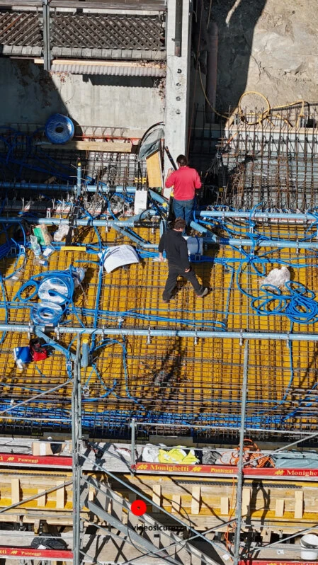 Vista aerea ravvicinata di due operai che lavorano su un solaio in cemento armato con armatura metallica e tubazioni elettriche in un cantiere edile